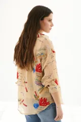 Camisa beige de manga larga con cuello clásico y cierre frontal con botones. Presenta bordados con motivos florales y geométricos en tonos azules, rojos y verdes.