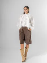 Camisa blanca de algodón italiano con cuello alto ajustable mediante lazo trasero, mangas abullonadas y un gran shabot frontal con volados en cascada.