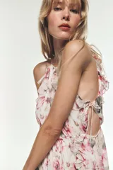 Vestido largo con estampado floral, cuello redondo y tirantes finos. Presenta elástico en la cintura con aberturas y lazadas laterales, volantes en el mismo tejido, forro interior a contraste y abertura frontal en el bajo. Cierre en la espalda con botón.