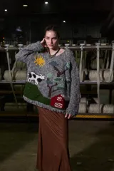 Sweater tejido de lana color gris con cuello redondo y puños acanalados. Presenta un diseño bordado a mano con motivos campestres: sol, vaca, árbol y granero.