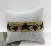Pulsera tejida con pequeñas cuentas de colores rojo y dorado, formando un patrón de estrellas doradas sobre fondo rojo.