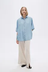 Camisa celeste de manga corta, corte holgado, con cuello camisero y cierre frontal con botones.