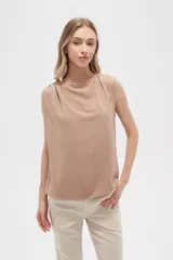 Blusa color beige de poliéster, sin mangas, con cuello asimétrico y detalle de drapeado en los hombros.