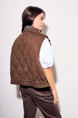 Chaleco reversible de algodón con acabado lavado y diseño acolchado con pespuntes ondulados. Presenta cuello alto con cordón ajustable, cierre frontal de cremallera y botones a presión, bolsillos delanteros tipo parche y cordón de ajuste en el bajo.