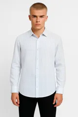 Camisa de algodón a rayas verticales celestes y blancas, con cuello clásico y cierre frontal con botones. De corte clásico y mangas largas con puños abotonados.