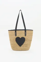 Bolso grande tipo tote de raffia color beige con aplique de corazón negro. Asas de mano y ribetes de cuero sintético negro.