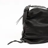 Cartera negra de cuero con textura granulada, forma rectangular y cierre superior con cremallera. Tiene una correa de hombro ajustable con apliques metálicos y detalles de cordones en los laterales.