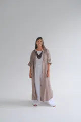 Camisola larga a rayas verticales color café, confeccionada en lino 100%. Tiene cuello camisero, mangas largas con botón ajustable y cierre frontal con botones.