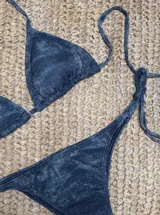 Conjunto de bikini azul con corpiño de triángulos movibles con almohadillas desmontables, que se ata al cuello y a la espalda. La bombacha es vedetina con tiritas a los costados para atar a medida de la cadera.