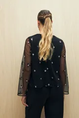 Blusa negra de tul bordado con pequeñas lentejuelas y mangas largas transparentes.