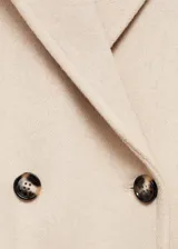 Abrigo de paño color beige, con cuello de solapa, doble botonadura y bolsillos con solapa.