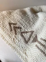 Manta de lana color crudo con bordados de flechas en color marrón.