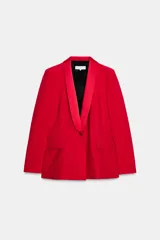 Blazer roja de corte recto, con cuello smoking de satén negro, mangas largas con hombreras, bolsillos frontales con solapa y cierre frontal con un botón.