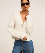 Cardigan corto color crema, de tejido tricot, con mangas largas y cierre frontal con lazos.