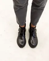 Bota corta de cuero color negro, estilo botín, con suela track gruesa y dos tiras ajustables con hebillas brillantes en el empeine.