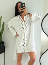 Vestido camisero blanco con aberturas geométricas en el frente, mangas largas con volados y bajo irregular.