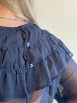 Blusa de gasa azul marino traslúcida con volados en los hombros y mangas largas abullonadas.