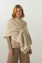 Ruana color crema de tejido de punto industrial con terminación en contraste de color. Tiene doble ojal para mantener el cruce.