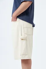 Bermuda carpenter de denim negro, corte relajado y largo a la rodilla, con costuras visibles y múltiples bolsillos funcionales.