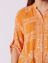 Camisa naranja con estampado cachemir, cuello mao, escote en V y cierre frontal con botones. Mangas 3/4 regulables con presilla y ruedo asimétrico.