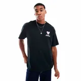 Camiseta negra de algodón con cuello redondo y mangas cortas. Presenta un estampado en el pecho con un corazón rosa y la palabra 'Nike' en cursiva blanca.