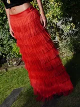 Falda larga color verde oliva con múltiples capas de flecos largos, creando un efecto texturizado. La falda tiene un tajo lateral.