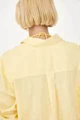 Camisa amarilla de tejido liviano de mezcla de lino y viscosa con cuello, botones adelante y canesú de doble capa con pliegue de caja en la espalda. Modelo de manga larga con bolsillo superior abierto, puños abotonados y bajo redondeado.