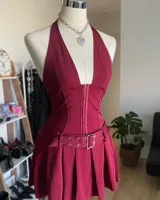 Vestido corto color borgoña con escote halter, cierre frontal con ganchos metálicos, falda plisada y cinturón con hebilla metálica.