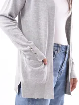 Saco color beige de tejido de punto, con cuello abierto, bolsillos frontales y mangas largas con detalle de botones en los puños.