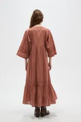 Vestido largo color marrón, con escote en V, mangas 3/4 y detalles de broderie en el pecho, mangas y falda. La falda tiene un volado en el ruedo.