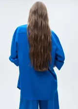 Camisa azul eléctrico de tejido fluido con mezcla de lino y lyocell, cierre frontal oculto, manga larga con puños abotonados, diseño recto, cuello camisero, diseño largo y dos bolsillos de solapa en la parte delantera.