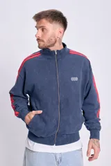 Campera deportiva con cierre frontal, cuello alto y puños y cintura acanalados. Color azul marino con efecto desgastado y dos franjas rojas a lo largo de las mangas. Presenta un pequeño logo bordado en el pecho.