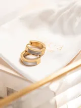 Aros tipo argolla pequeños de acero quirúrgico con baño de oro 18k, con un inserto rectangular de nácar o material nacarado en el centro.