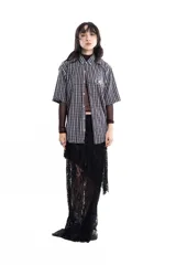 Camisa unisex de manga corta con estampado a cuadros en tonos verde, negro, blanco y morado. Presenta un corte boxy y un estampado en serigrafía en el pecho.