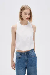 Blusa blanca de algodón sin mangas, con cuello a la base, abertura en la espalda y lazo ajustable.