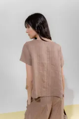 Blusa de lino color beige con rayas verticales negras, corte recto, escote redondo y mangas cortas.