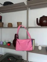 Cartera tipo bandolera color rosa chicle, de lona semi impermeable, con cierre metálico, forrería de gross y bolsillo interno. Tiene tira regulable para usar al hombro, cruzada o como riñonera.