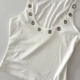 Musculosa blanca de punto canalé con cuello redondo y detalle de ojales metálicos en el escote y sisas.