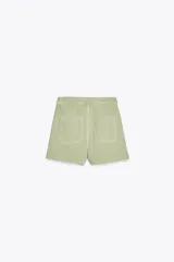 Falda pantalón corta color crudo, de tiro alto con delantero cruzado y cierre con cremallera oculta y botones.