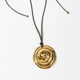 Collar con dije dorado en forma de espiral irregular, colgando de un cordón negro.