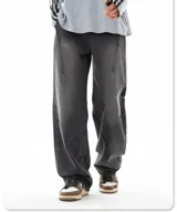 Jean de mezclilla color negro lavado, corte ancho y holgado, caracterizado por costuras diagonales pronunciadas en la parte delantera de las piernas que crean un efecto de paneles o cortes asimétricos.