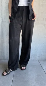 Pantalón negro de vestir con finas rayas verticales blancas, corte recto y tiro alto.