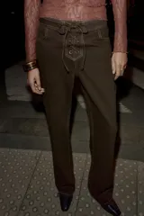 Jeans de tiro alto color marrón oscuro, con pernera recta y detalle de cordones cruzados en la parte delantera central. Presenta costuras contrastantes en color claro.