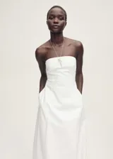 Vestido strapless blanco de corte recto y largo midi, con bolsillos laterales. Incluye collar plateado con dije de llave.