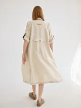 Vestido camisero de lino color beige, de corte recto, con cuello camisero, mangas cortas con puños y bolsillo de parche en la espalda.