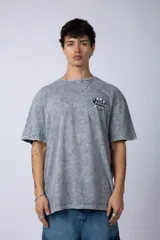 Remera gris con efecto acid wash, corte holgado y estampa frontal con una mano sosteniendo el mundo VCP.