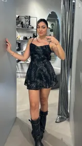 Vestido corto negro con breteles finos y falda evasé. Presenta un estampado de lunares plateados.