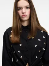 Camisa cropped negra de algodón con botones frontales, lazos para atar en la cintura, elástico en el bajo y apliques de pedrería.