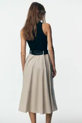 Vestido midi con falda beige con botones y cuerpo negro de cuello alto y sin mangas. Incluye cinturón negro con hebilla plateada.
