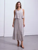 Vestido largo sin mangas, con estampado a rayas verticales en tonos beige, marrón y blanco. Tiene escote redondo y corte a la cintura con punto smock.